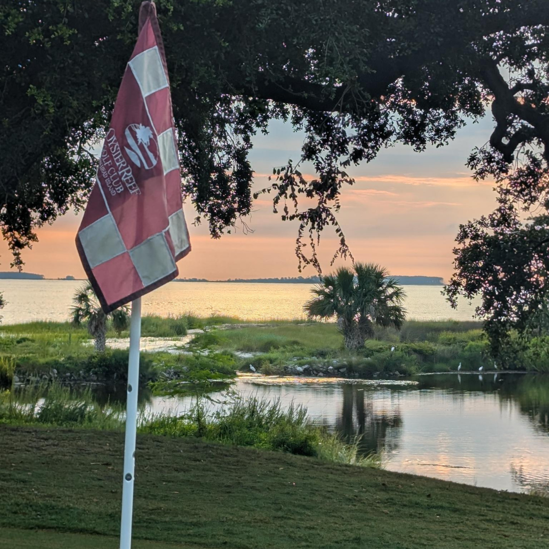 Oyster Reef golf course at sunset with trees, water, and a green